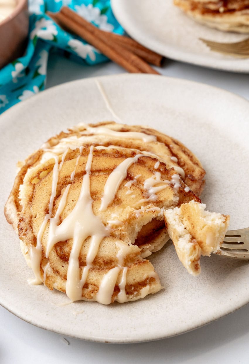 two cinnamon roll pancakes on a white plate with a silver fork resting on the side