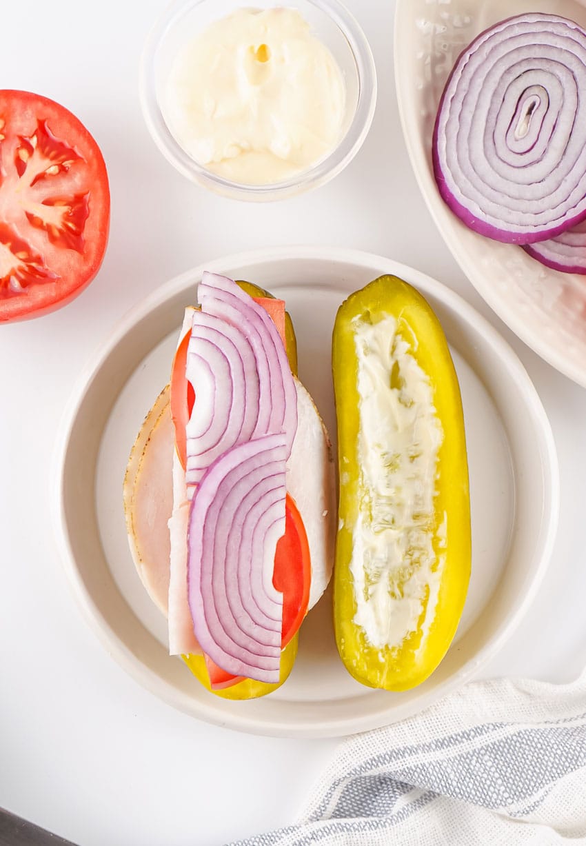 sliced turkey and layered veggies on a mayo slathered dill pickle on a white plate