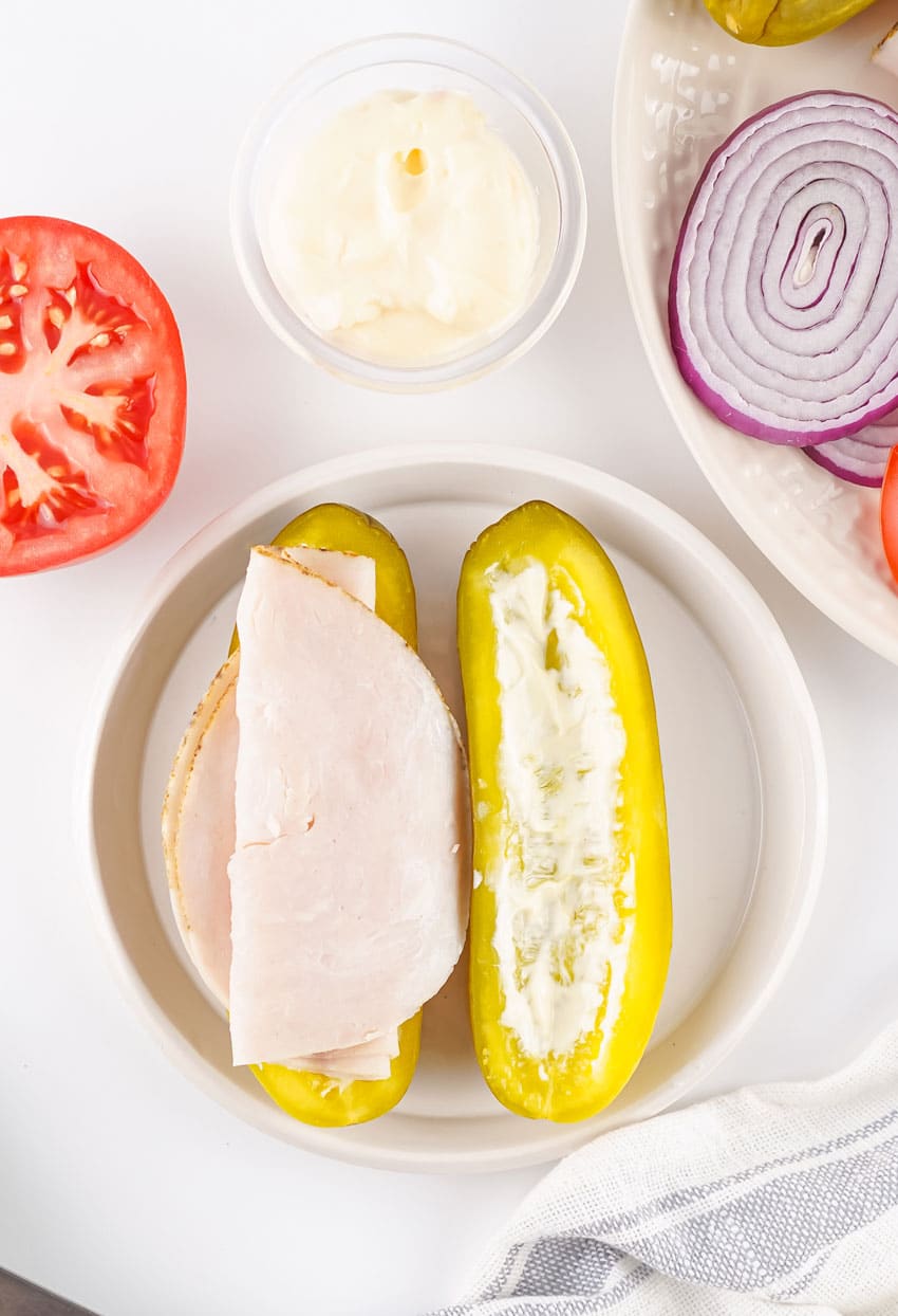 sliced turkey on a mayo slathered dill pickle on a white plate