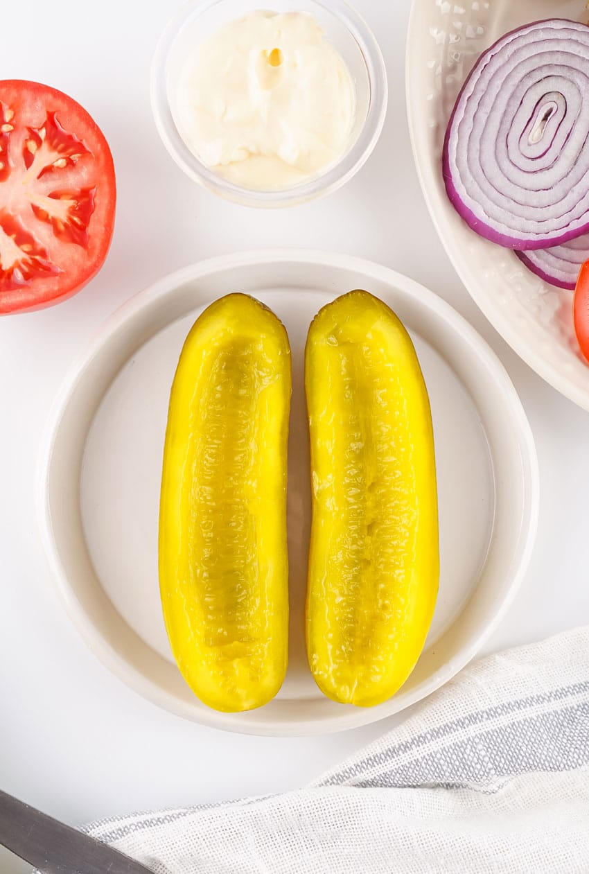 two hollowed out halves of a large dill pickle side by side on a white plate