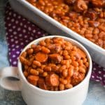hotdogs and beans casserole in a white mug next to a white baking dish
