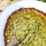 a wooden spoon scooping hot pesto dip out of a white serving dish