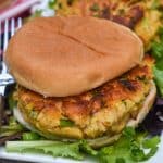 a crispy tuna patty on a hamburger bun resting on a bed of lettuce leaves on a white serving platter