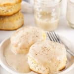 homemade white gravy over two fluffy biscuits on a white plate
