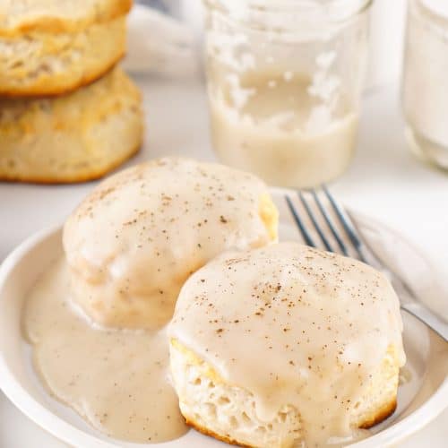 homemade white gravy over two fluffy biscuits on a white plate