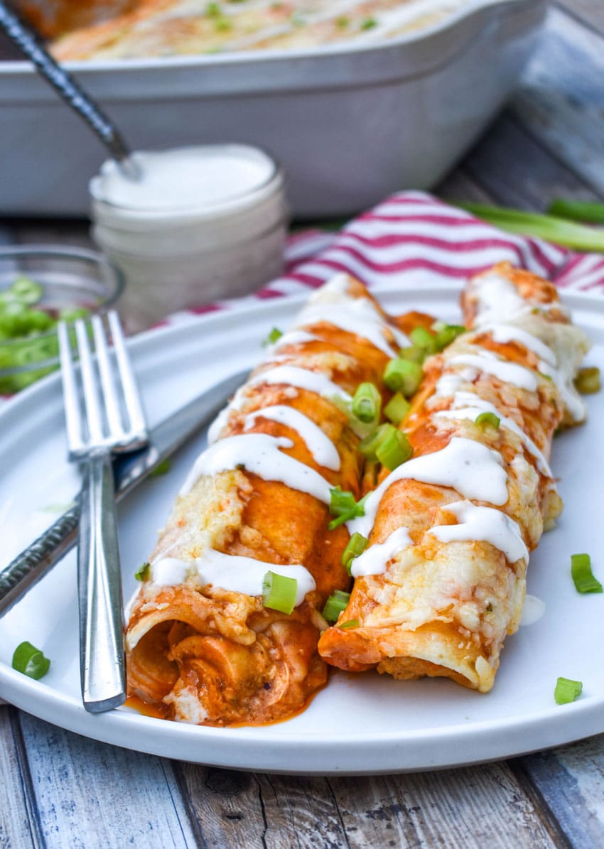two buffalo chicken enchiladas topped with a drizzle of ranch dressing and sliced green onions on a white plate