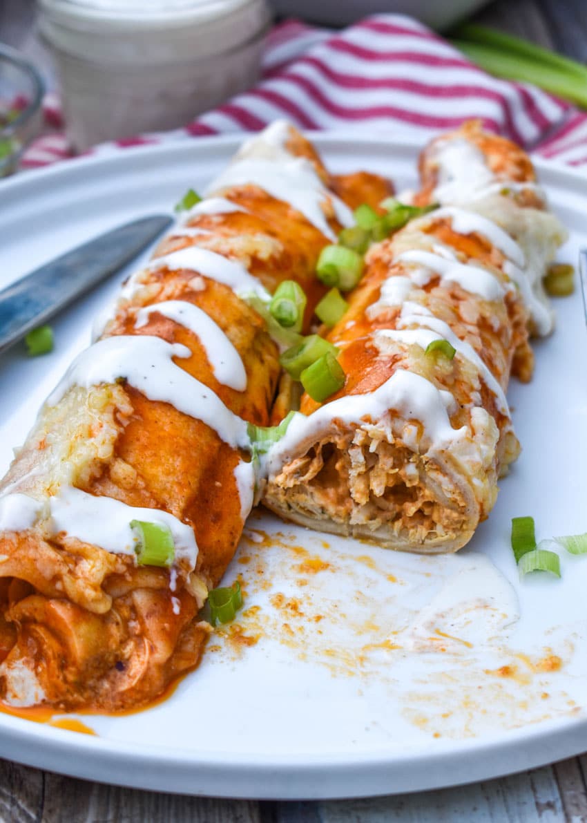 two buffalo chicken enchiladas topped with a drizzle of ranch dressing and sliced green onions on a white plate