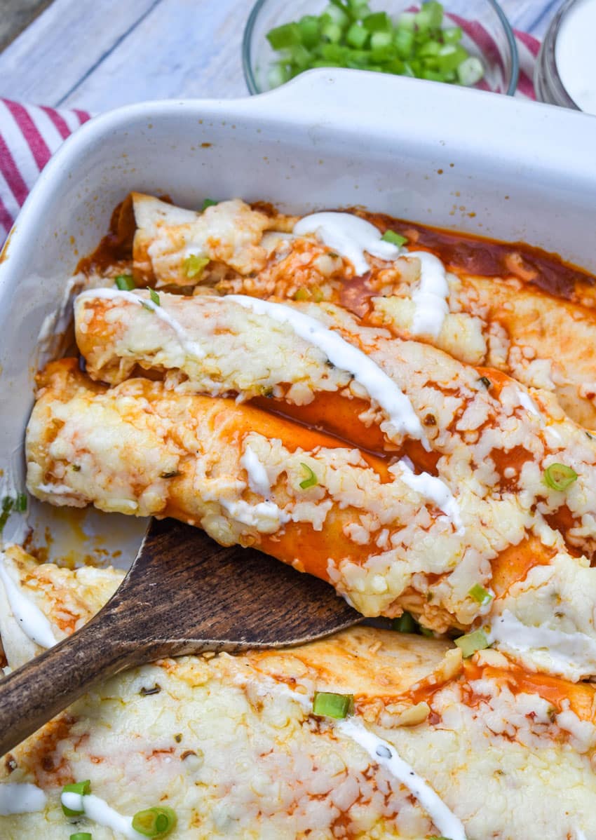 a wooden spatula scooping buffalo chicken enchiladas out of a white baking dish