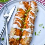 two buffalo chicken enchiladas topped with a drizzle of ranch dressing and sliced green onions on a white plate