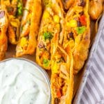 cut southwestern egg rolls on a metal tray with a glass bowl of cilantro sour cream on the side