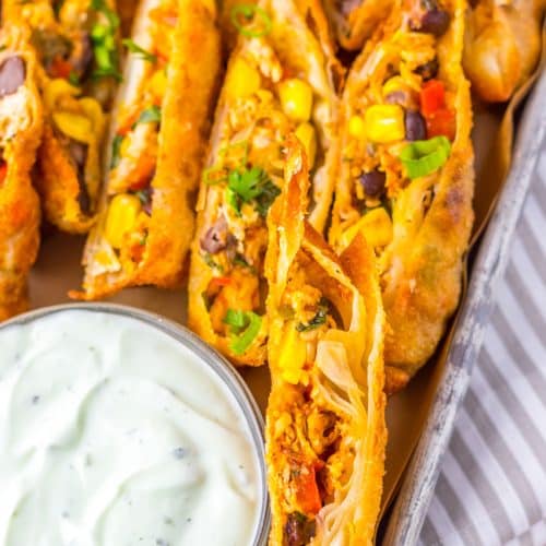 cut southwestern egg rolls on a metal tray with a glass bowl of cilantro sour cream on the side