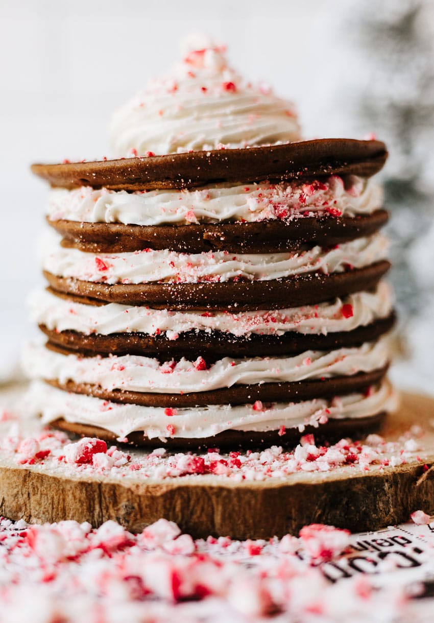 a stack of peppermint pancakes on a wooden cutting board surrounded by peppermint candy pieces