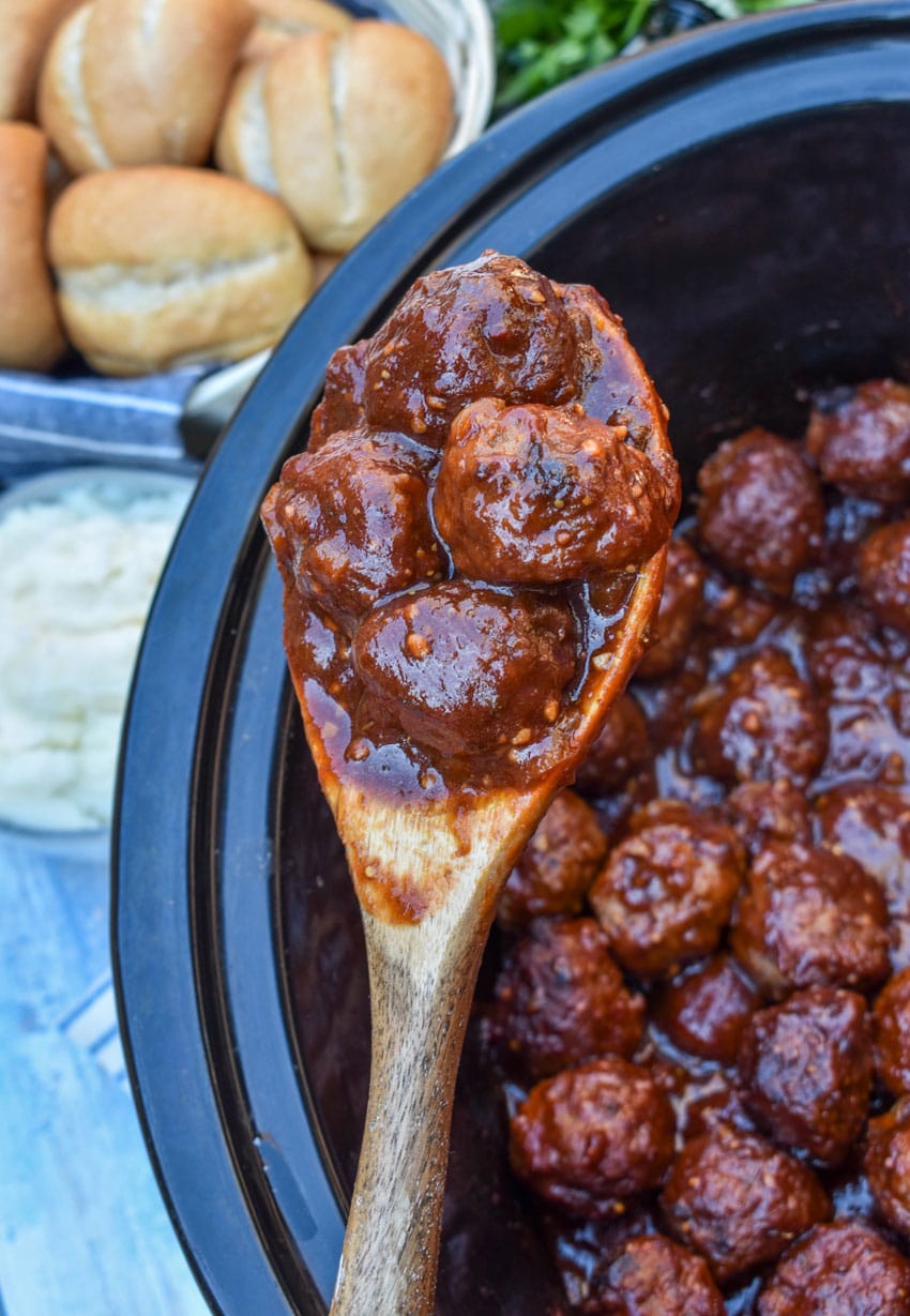 a wooden spoon holding up a scoop of slow cooker guinness meatballs