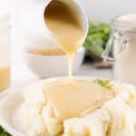 homemade brown gravy mix being poured over mashed potatoes on a white plate
