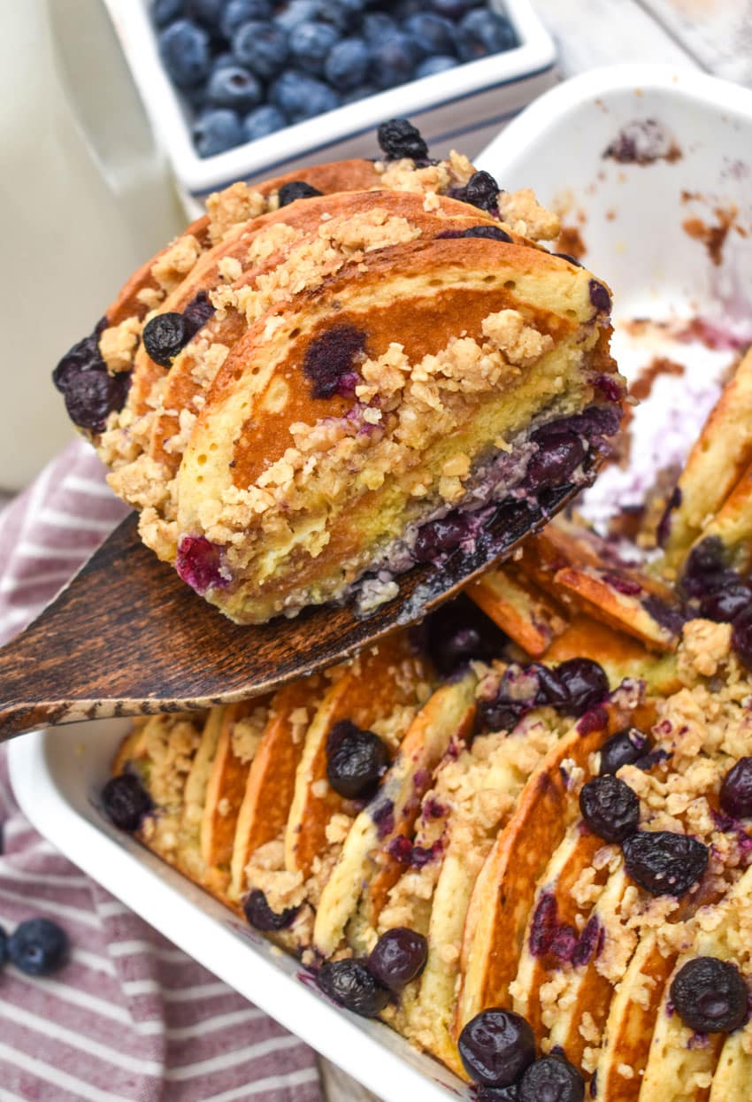 A WOODEN SPATULA HOLDING UP A SLICE OF BLUEBERRY PANCAKE CASSEROLE