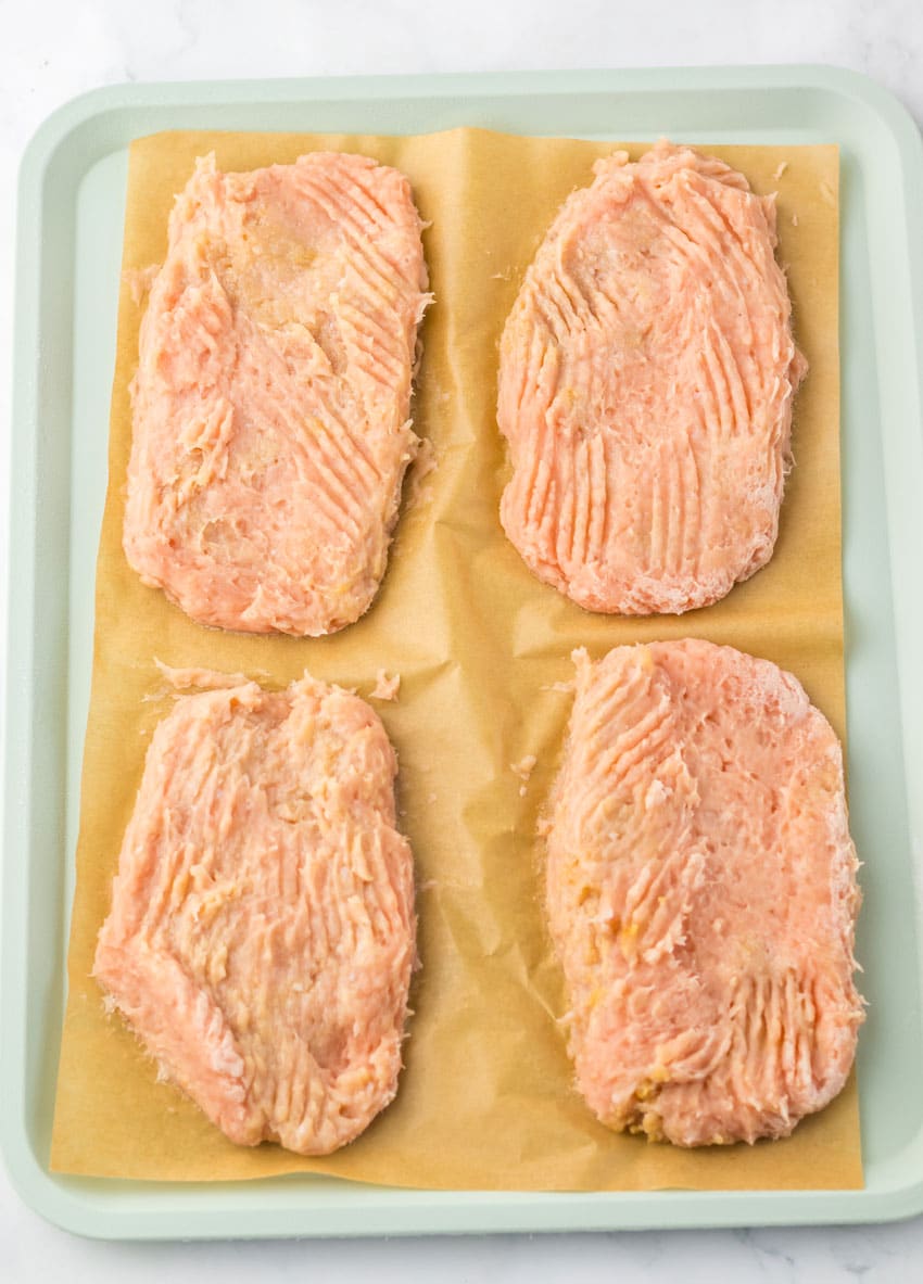 four ground chicken patties on a sheet of brown parchment paper