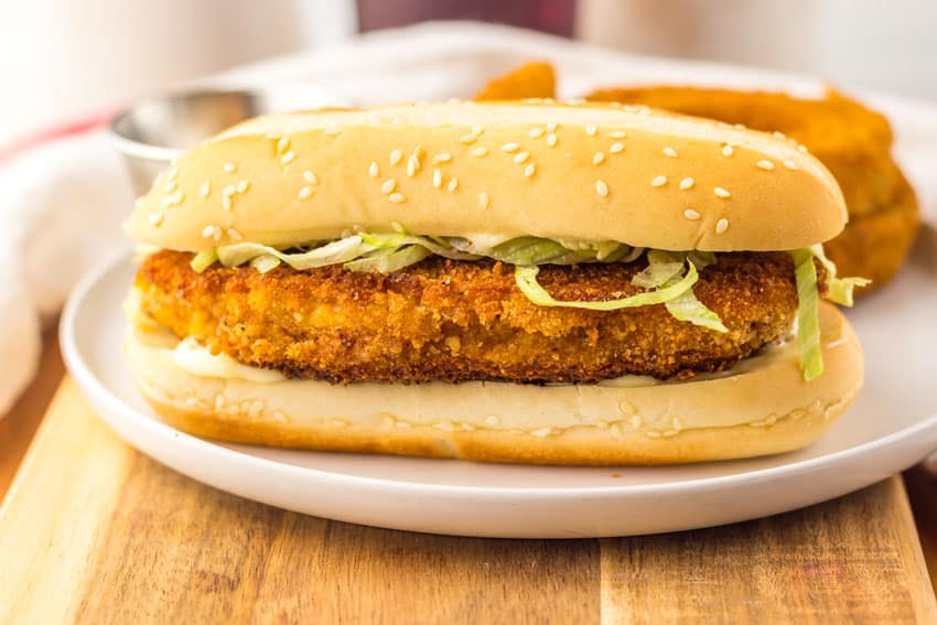 copycat burger king original chicken sandwich on a white plate with fried onion rings in the background