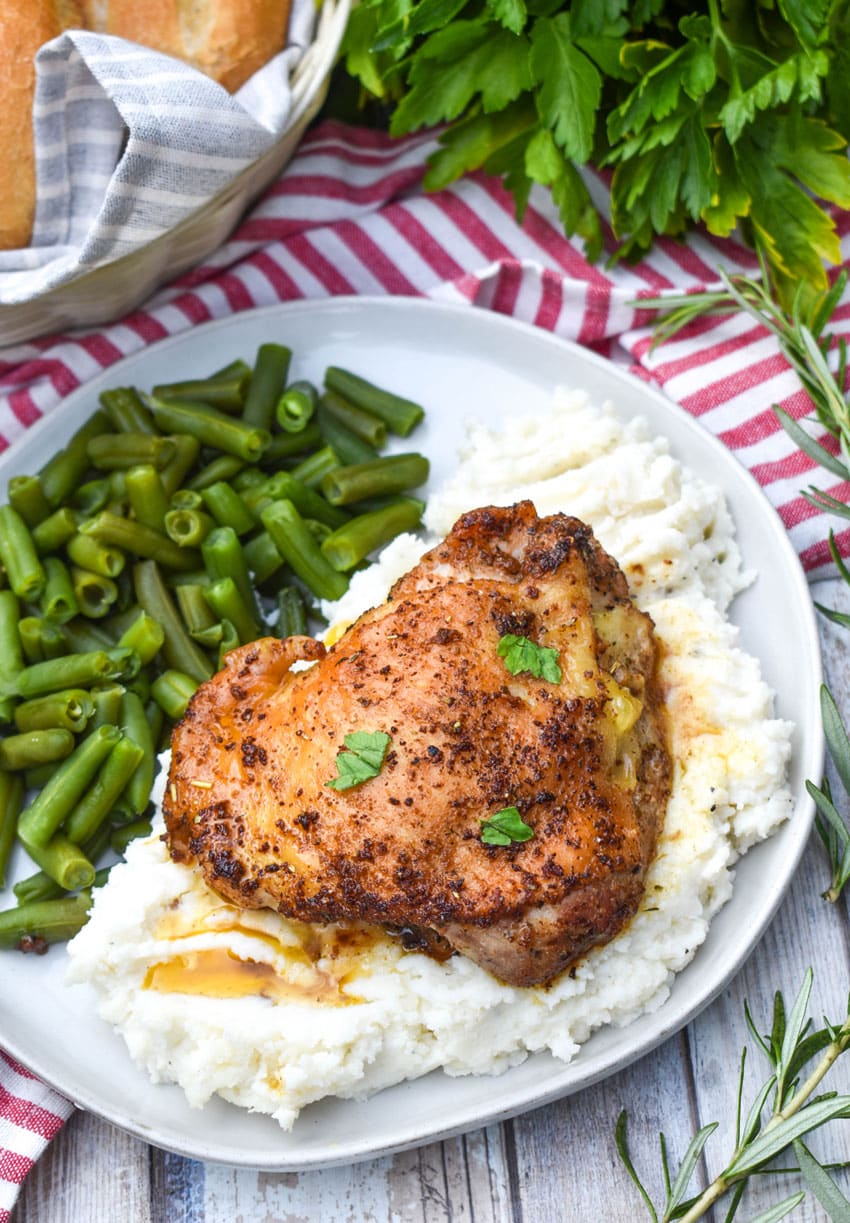 a crispy italian chicken thigh over mashed potatoes on a gray dinner plate with cooked green beans on the side