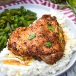 a crispy italian chicken thigh over mashed potatoes on a gray dinner plate with cooked green beans on the side