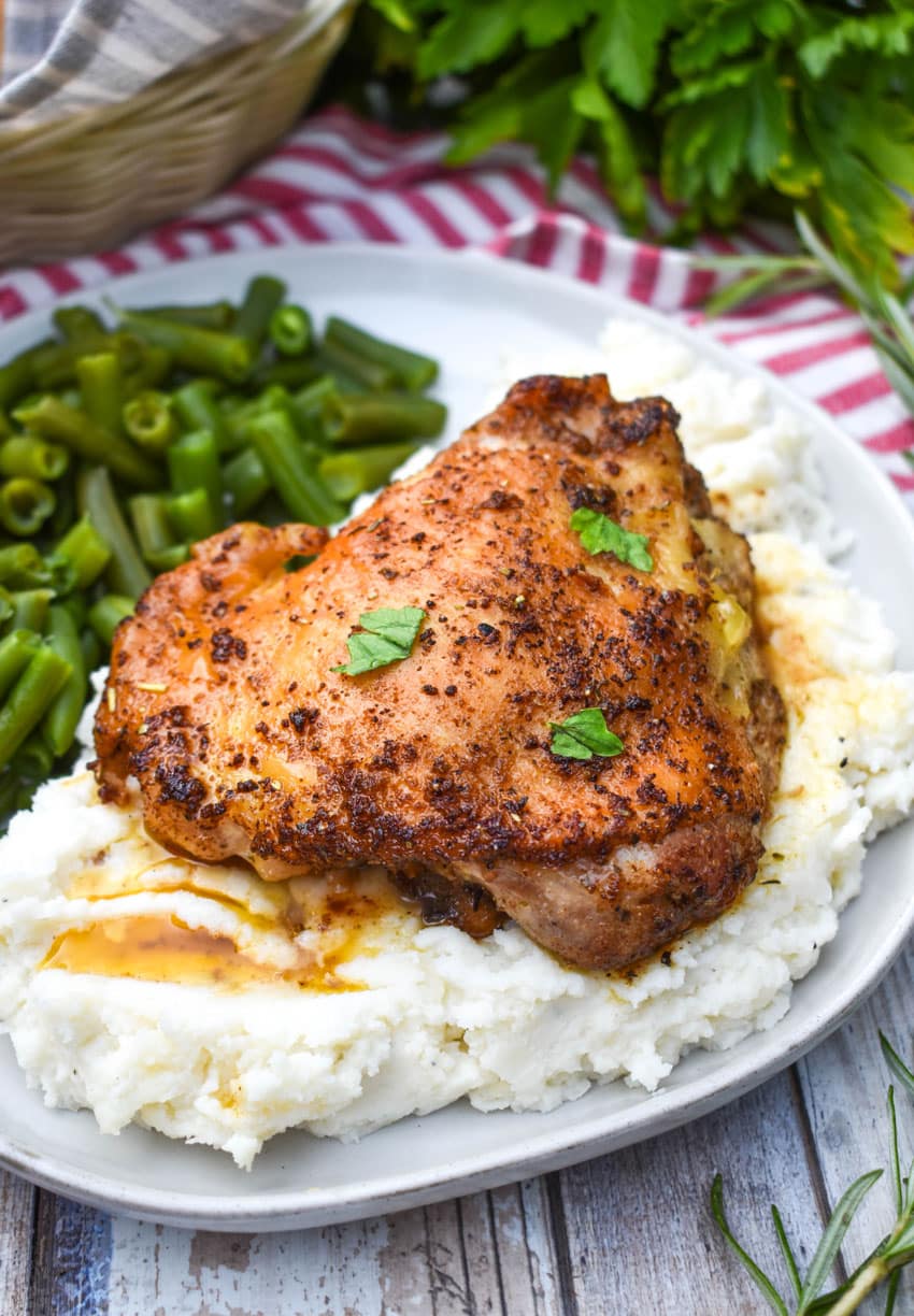 a crispy italian chicken thigh over mashed potatoes on a gray dinner plate with cooked green beans on the side
