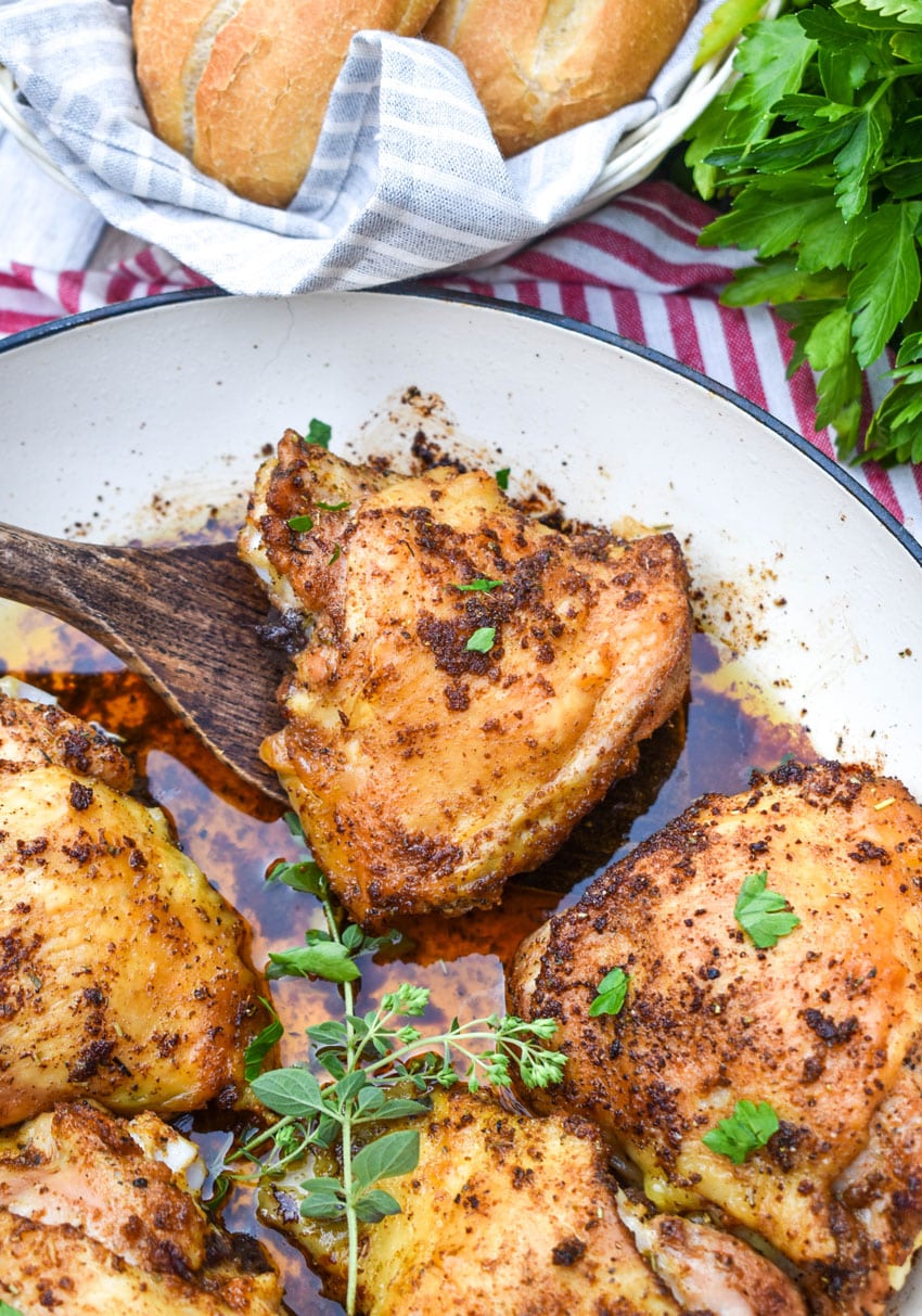 a wooden spatula scooping a crispy italian chicken thigh out of a large white cast iron skillet