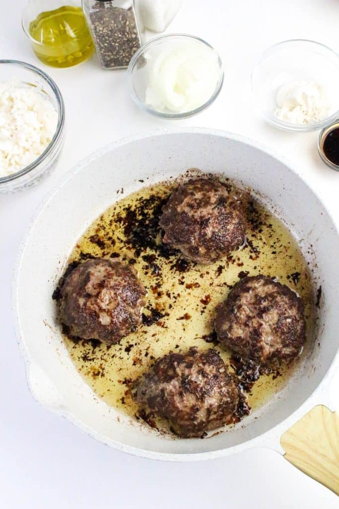 homemade hamburgers sautéing in a a white skillet