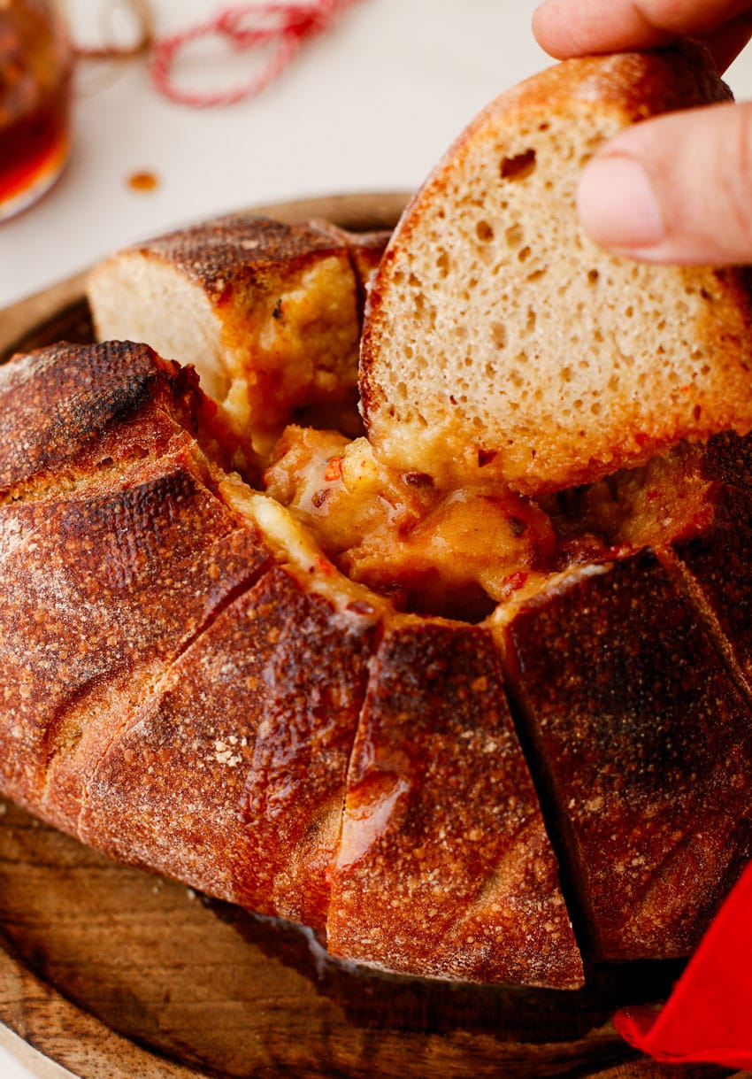 a hand dipping a slice of bread into a melted hot honey butter candle in a bread bowl