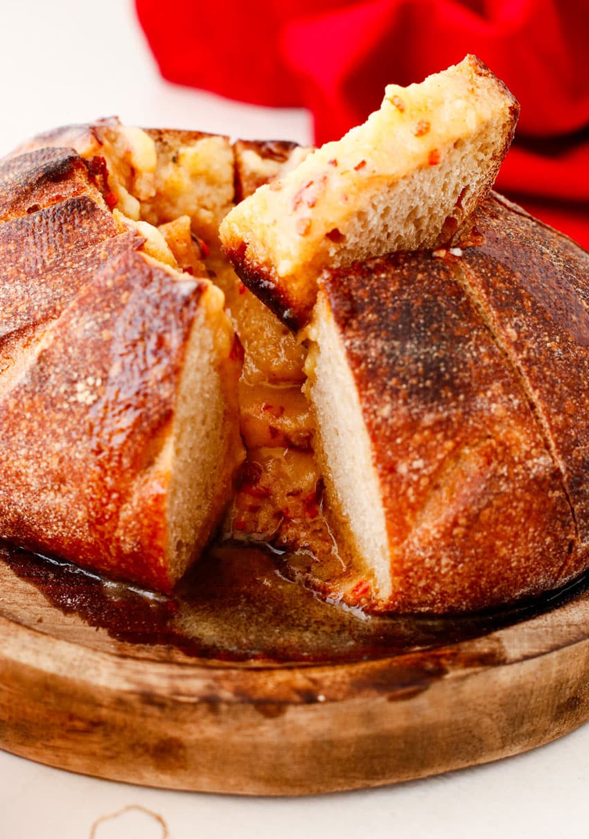 a hand dipping a slice of bread into a melted hot honey butter candle in a bread bowl
