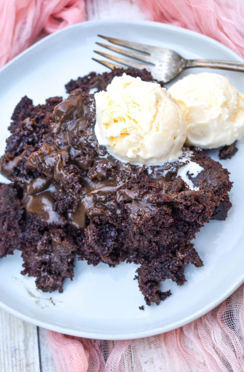 slow cooker chocolate lava cake topped with two scoops of melting vanilla ice cream on a gray plate