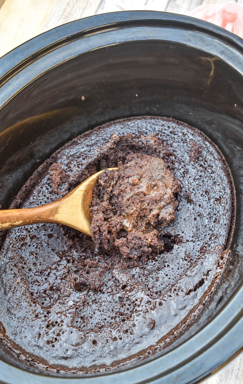 a wooden spoon scooping chocolate lava cake out of a black crockpot