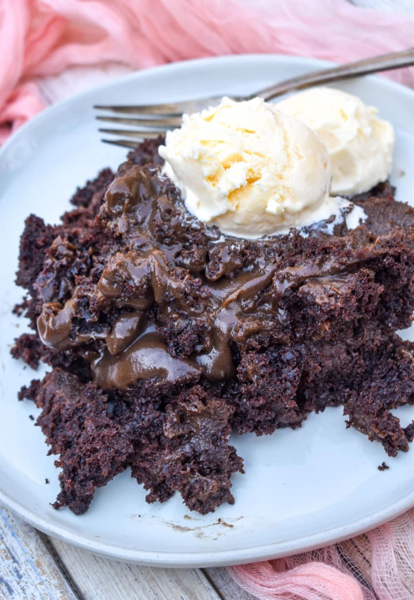 slow cooker chocolate lava cake topped with two scoops of melting vanilla ice cream on a gray plate