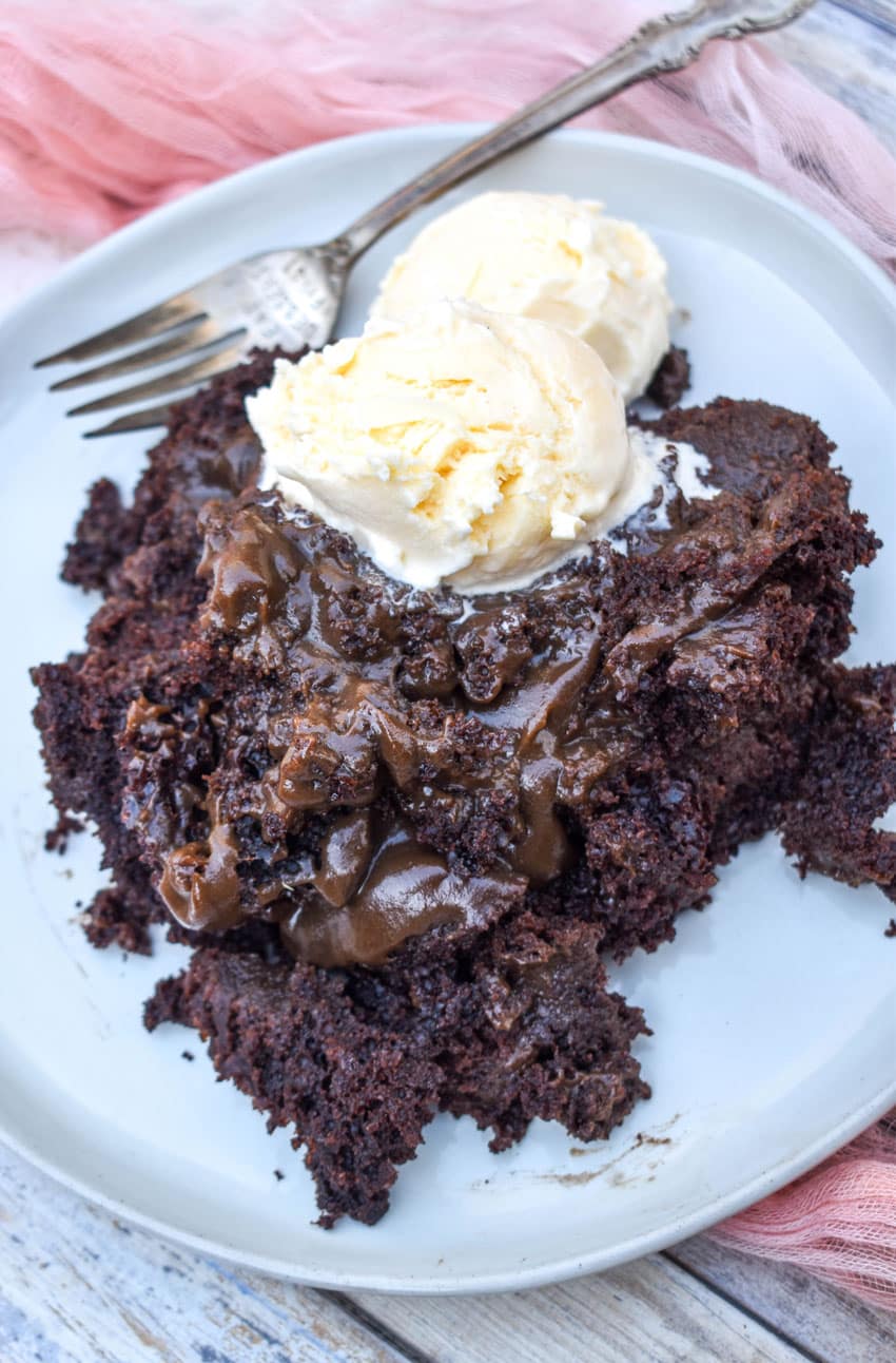 slow cooker chocolate lava cake topped with two scoops of melting vanilla ice cream on a gray plate