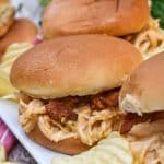 slow cooker garlic parmesan chicken sandwiches on a white serving platter with potato chips in the background