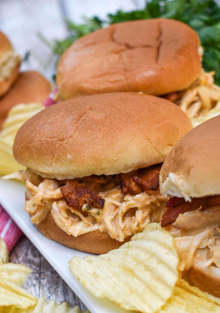 slow cooker garlic parmesan chicken sandwiches on a white serving platter with potato chips in the background