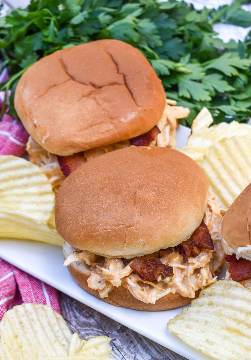 slow cooker garlic parmesan chicken sandwiches on a white serving platter with potato chips in the background