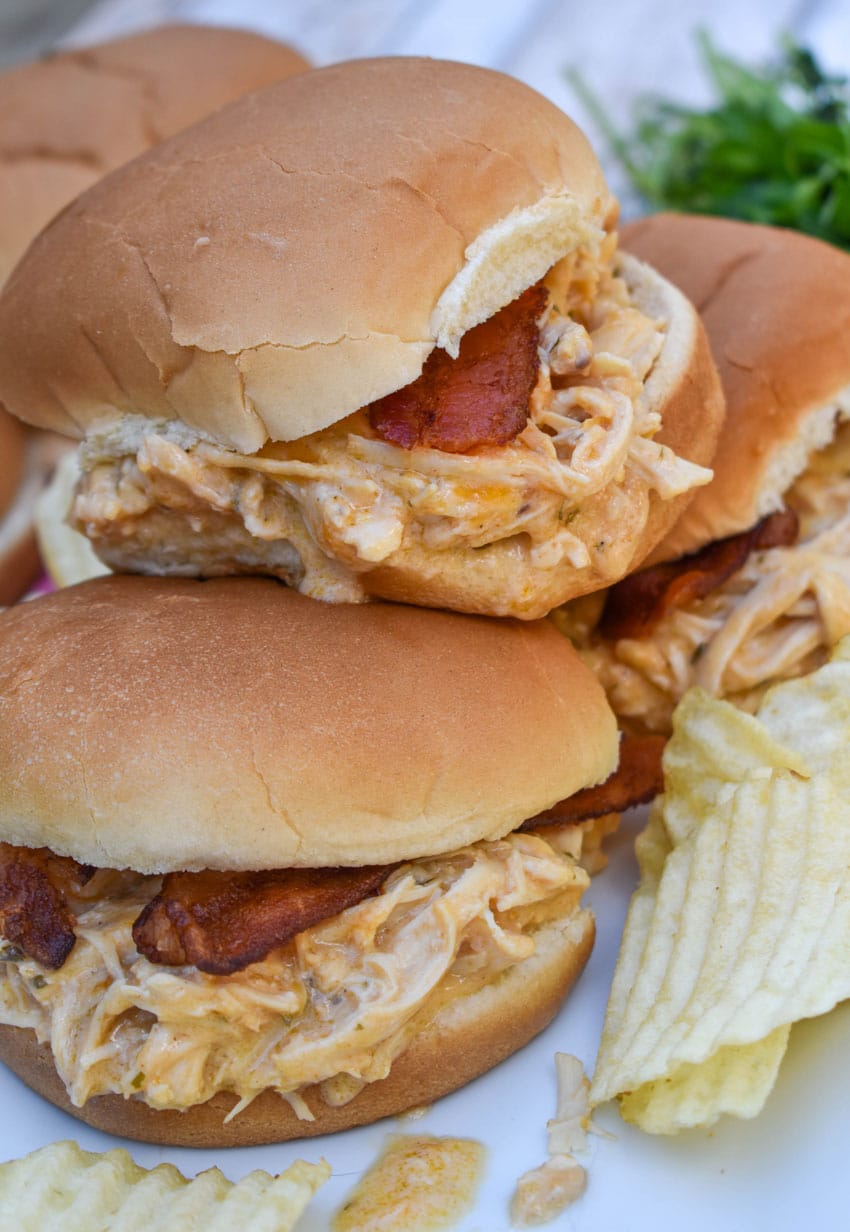 slow cooker garlic parmesan chicken sandwiches on a white serving platter with potato chips in the background