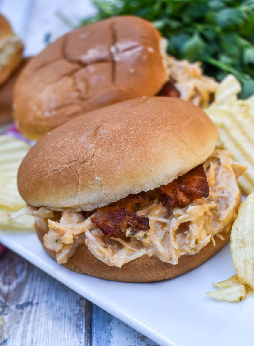 slow cooker garlic parmesan chicken sandwiches on a white serving platter with potato chips in the background