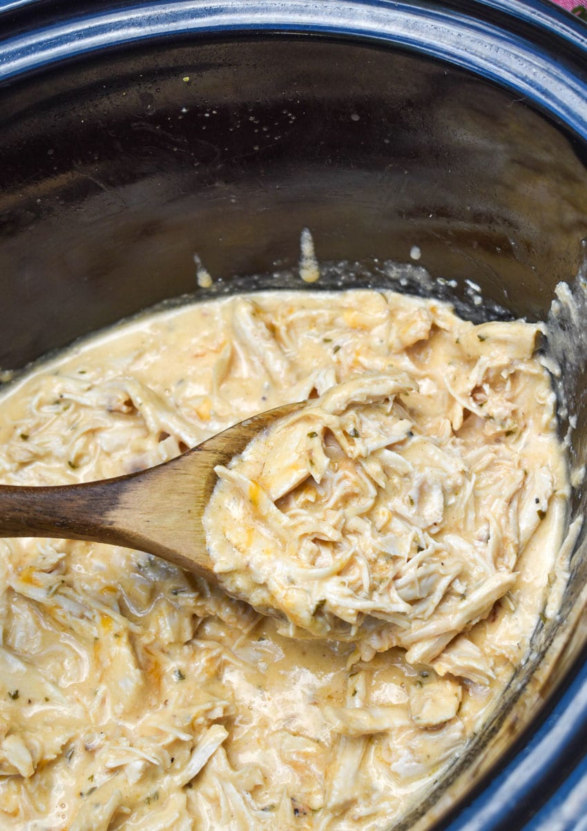 a wooden spoon scooping shredded garlic parmesan chicken out of a black crockpot