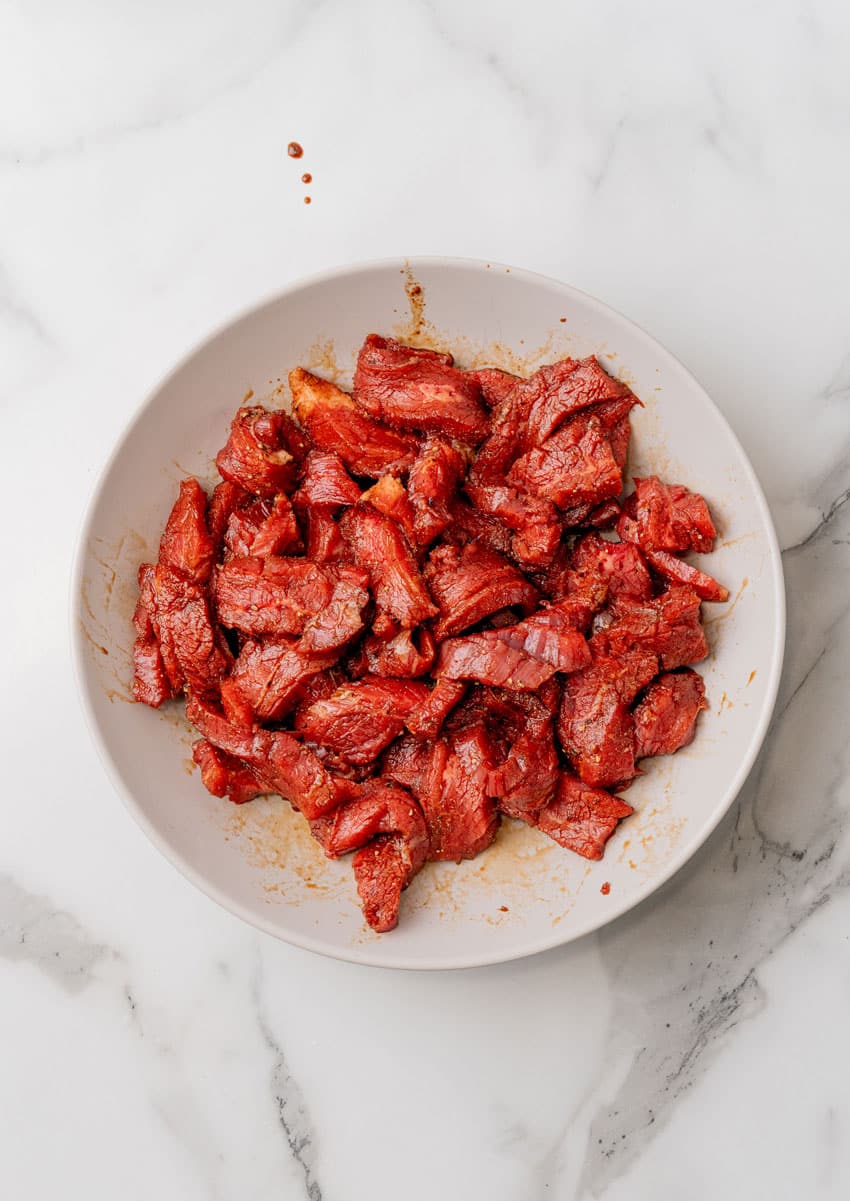 strips of beef marinading in a shallow white bowl