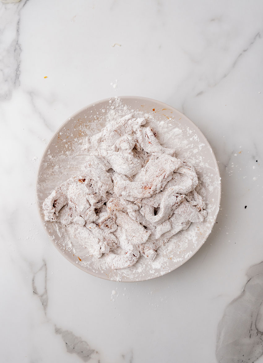 cornstarch coated strips of beef in a shallow white bowl