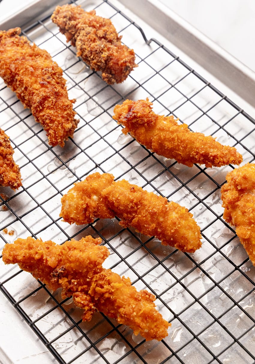 freshly fried strips of captain crunch chicken draining on a wire rack
