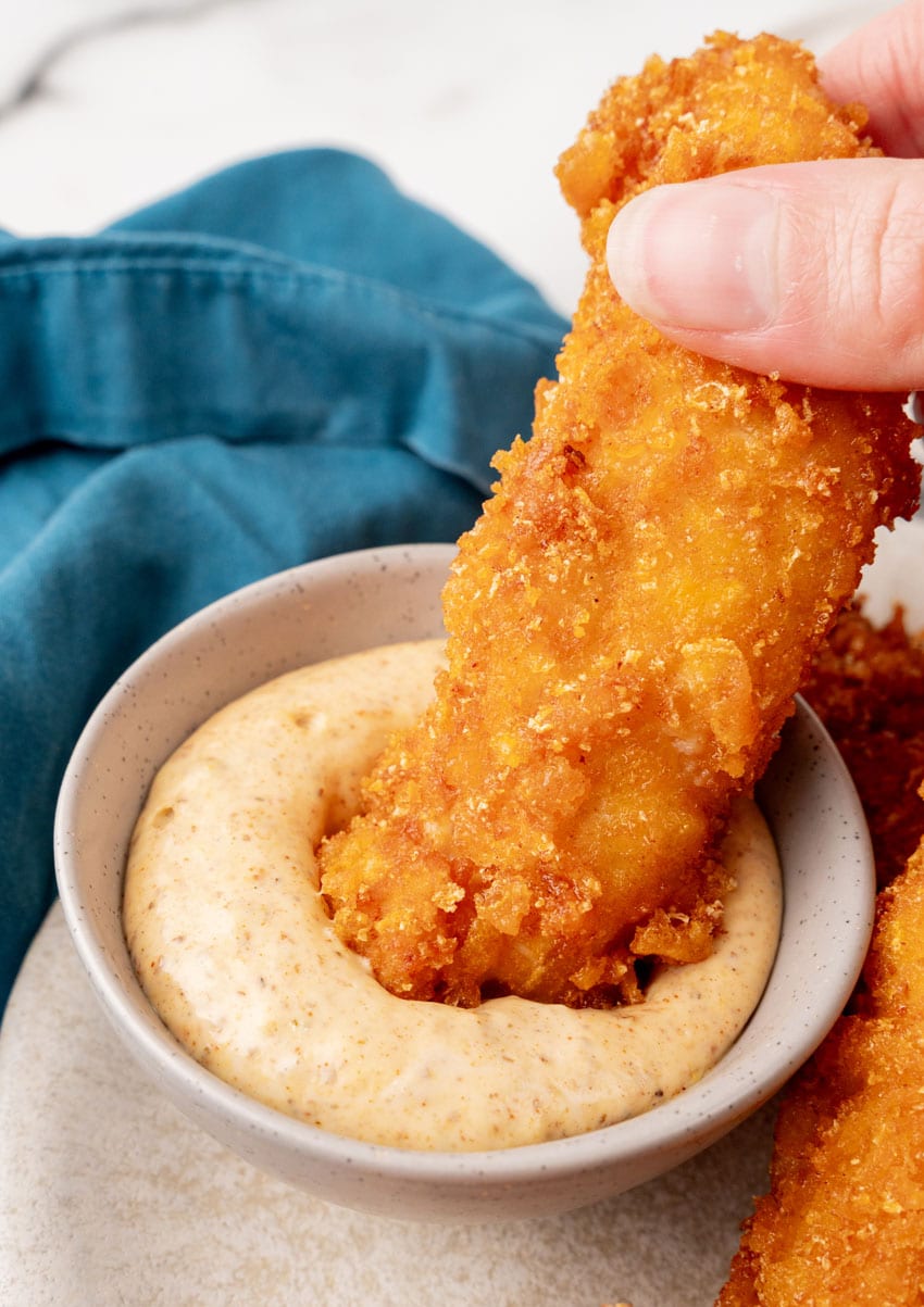 a copycat planet hollywood captain crunch chicken strips being dipped in a creamy orange sauce