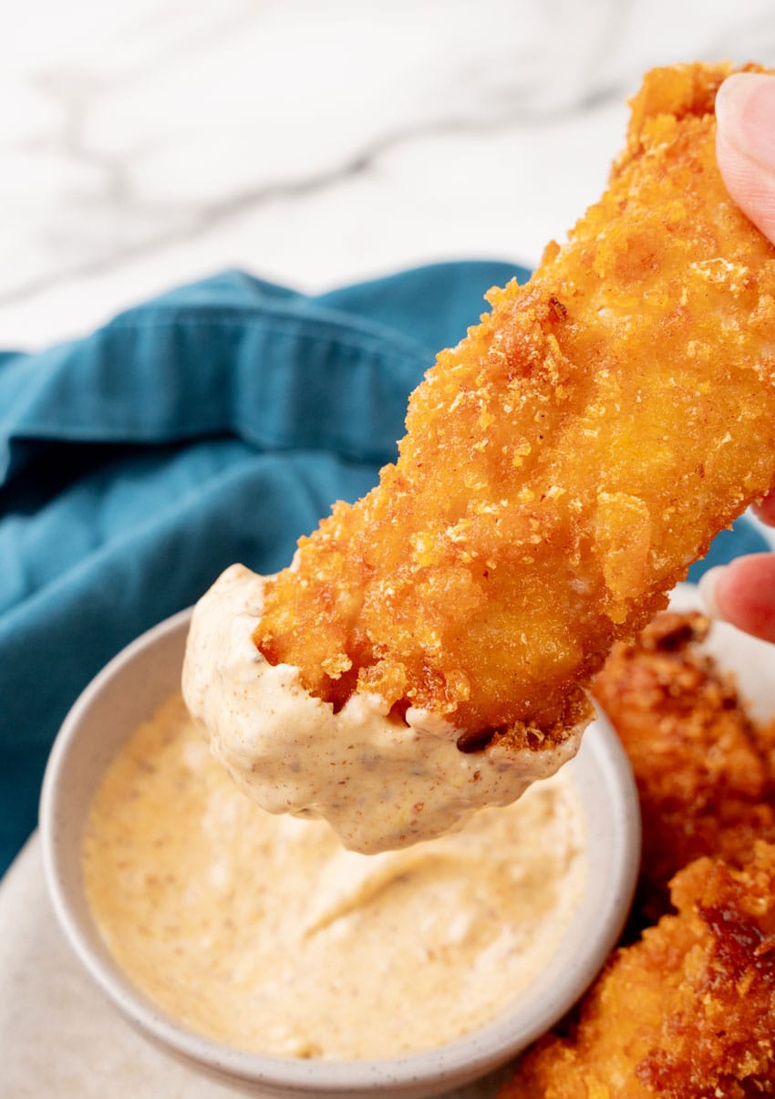 a copycat planet hollywood captain crunch chicken strips being dipped in a creamy orange sauce