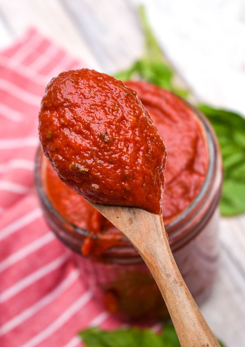 a wooden spoon scooping 5 minute homemade pizza sauce out of a glass jar