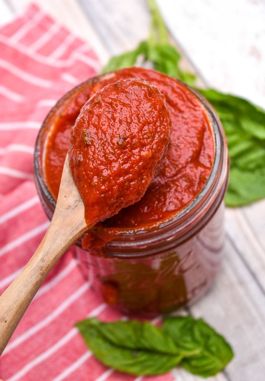 a wooden spoon scooping 5 minute homemade pizza sauce out of a glass jar