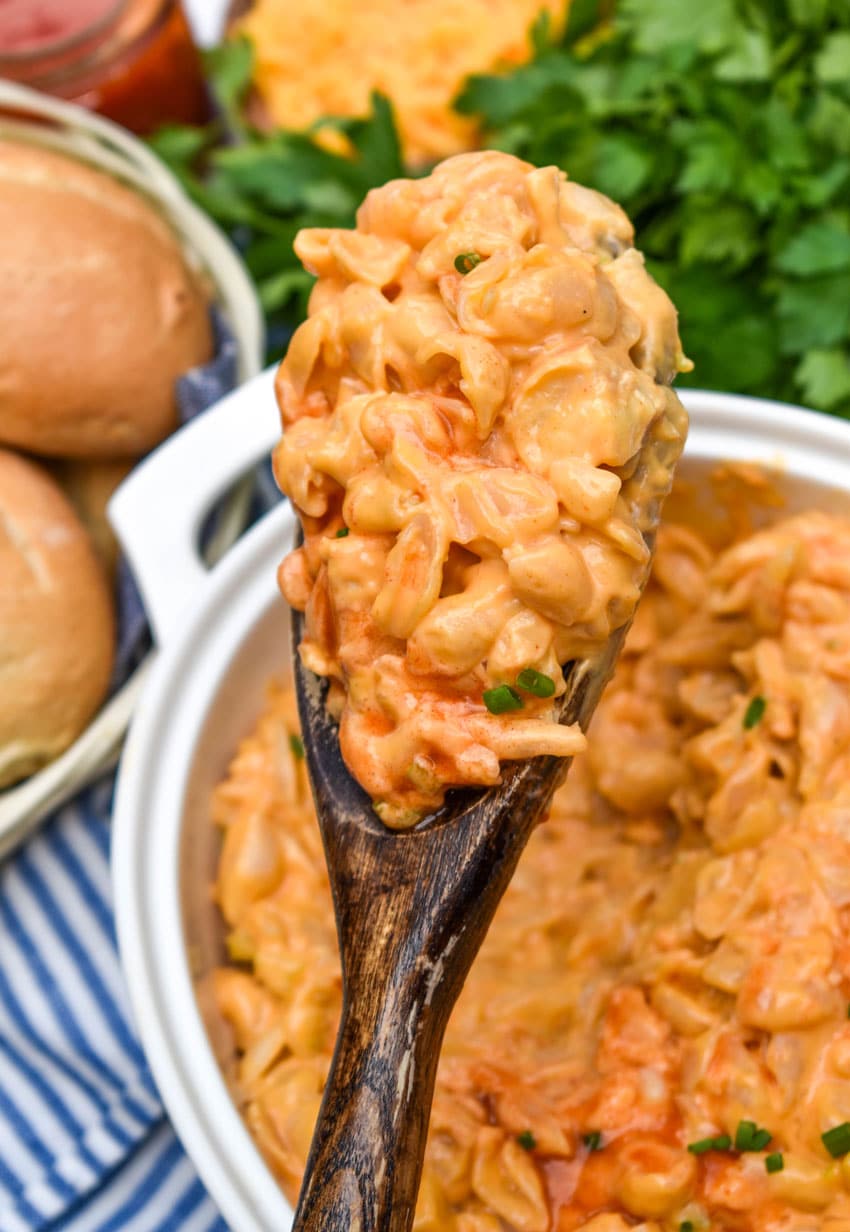 a wooden spoon holding up a scoop of buffalo mac and cheese from a box