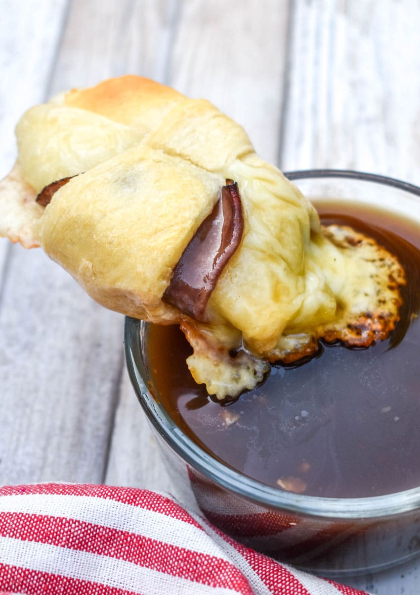 a french dip crescent roll being dipped in a small bowl filled with au jus sauce
