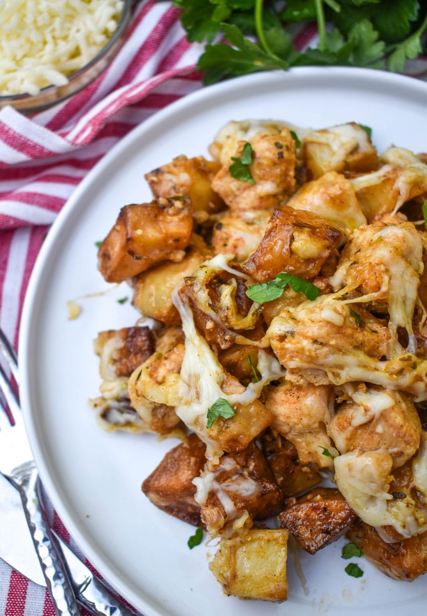 cheesy garlic parmesan chicken and potatoes on a white plate