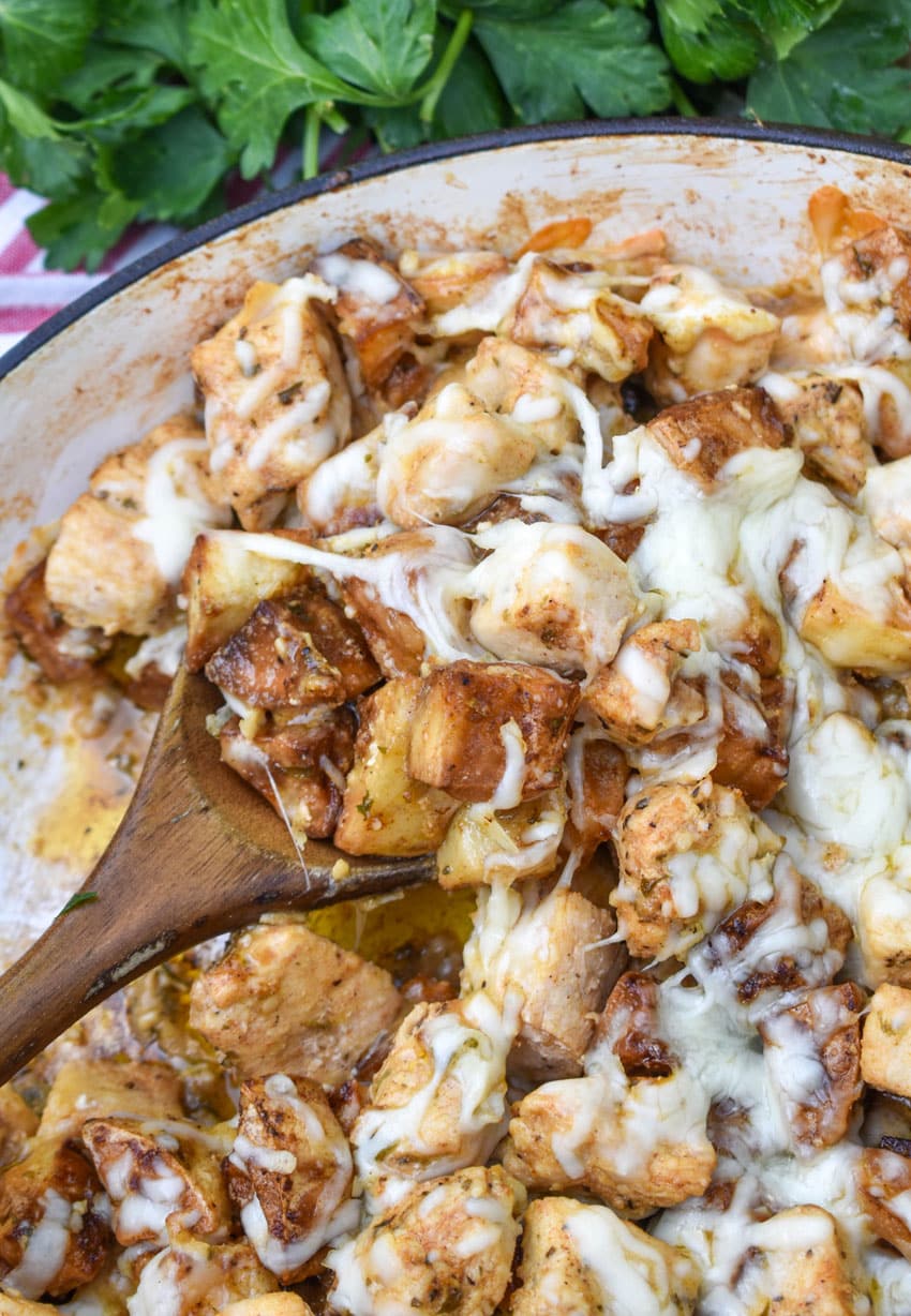 a wooden spoon scooping cheesy garlic parmesan chicken and potatoes out of a large skillet