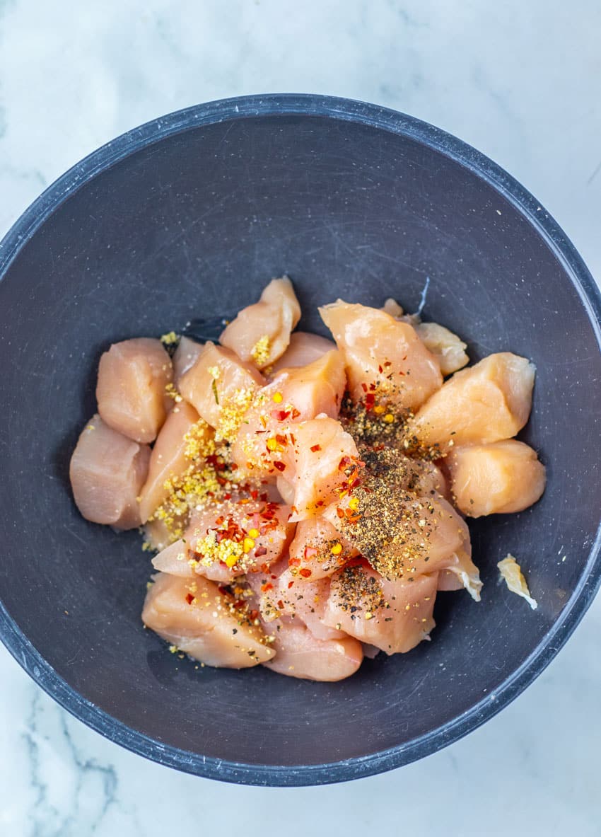 CHICKEN CHUNKS AND SEASONING IN A BLACK MIXING BOWL